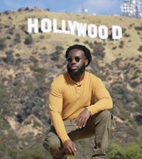 a black man crouching in front of the hollywood sign